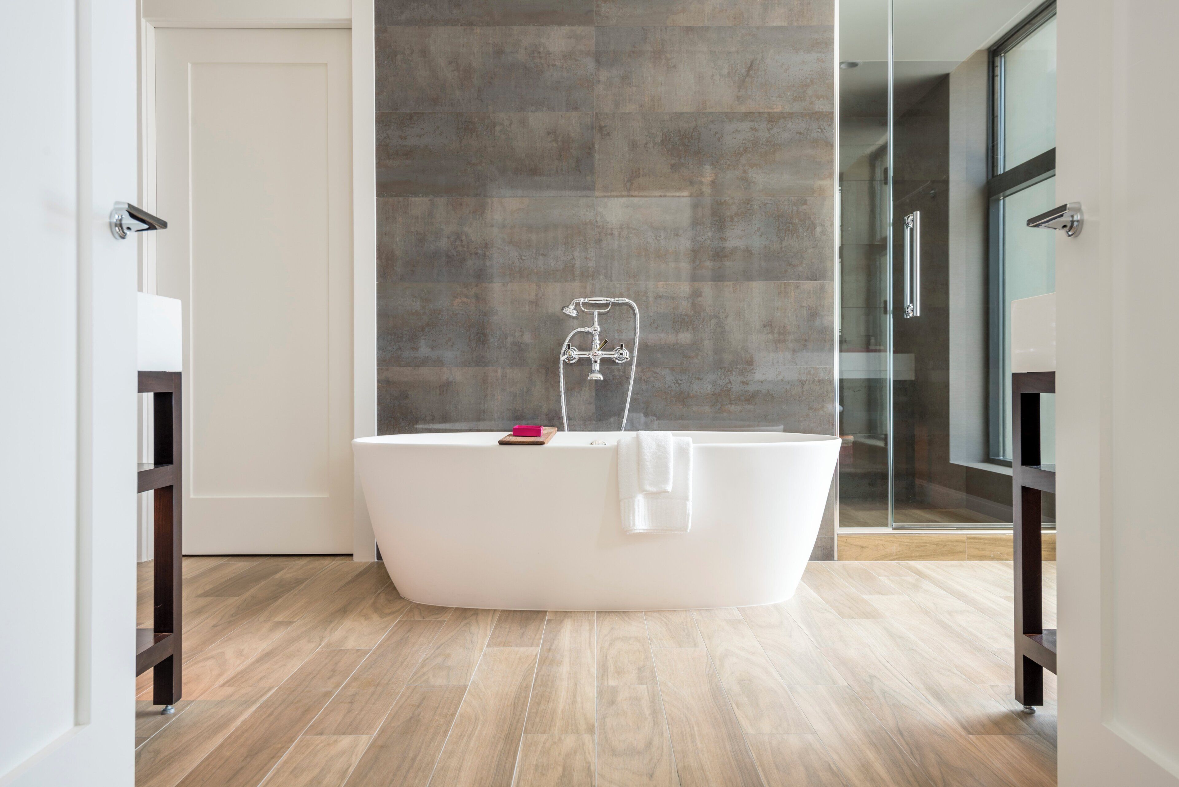 Une salle de bain moderne avec une baignoire sur pieds, une douche à l’italienne avec des parois en verre et un plancher en bois.