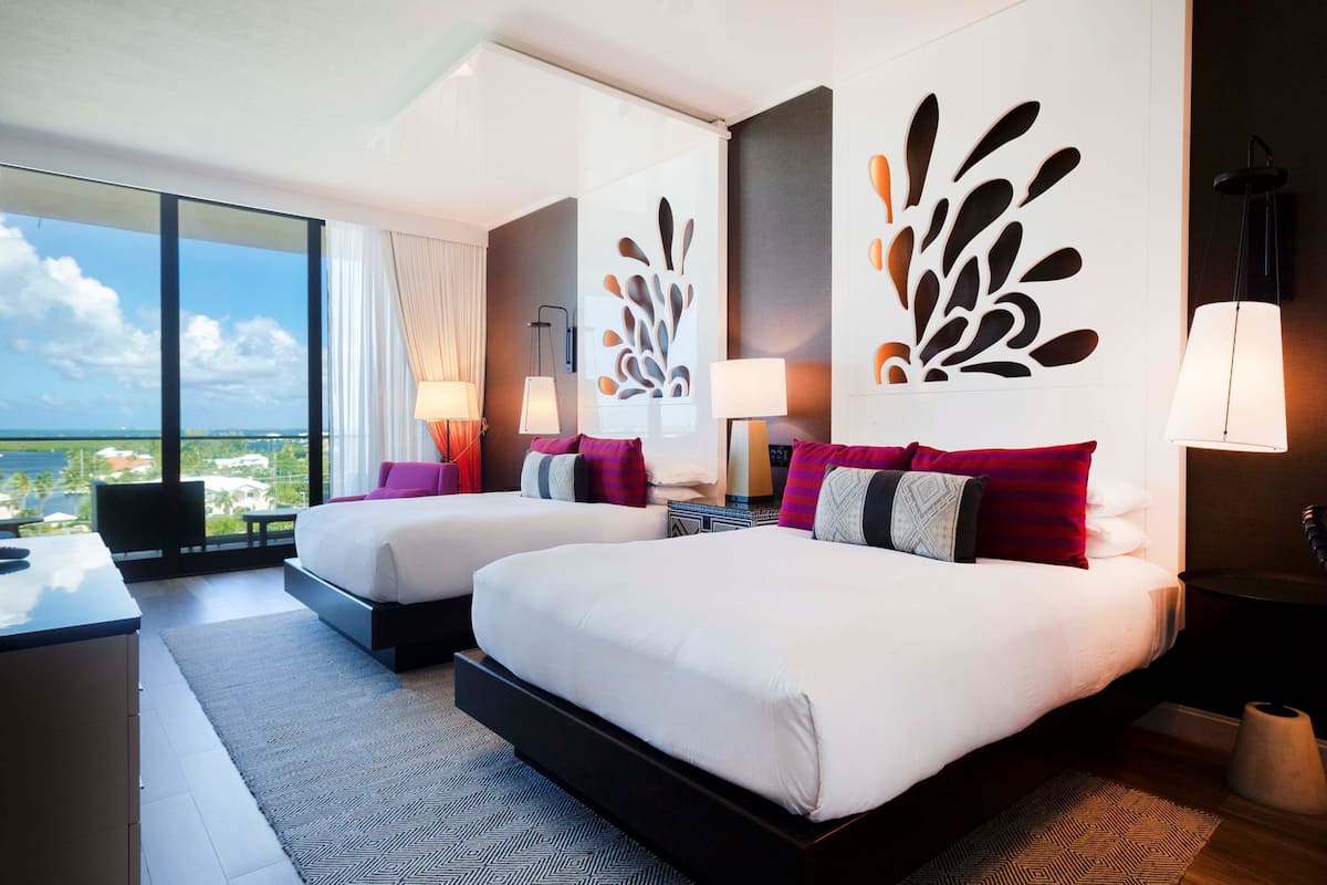 A hotel room with two beds, a desk, and a large window with a view of the city.