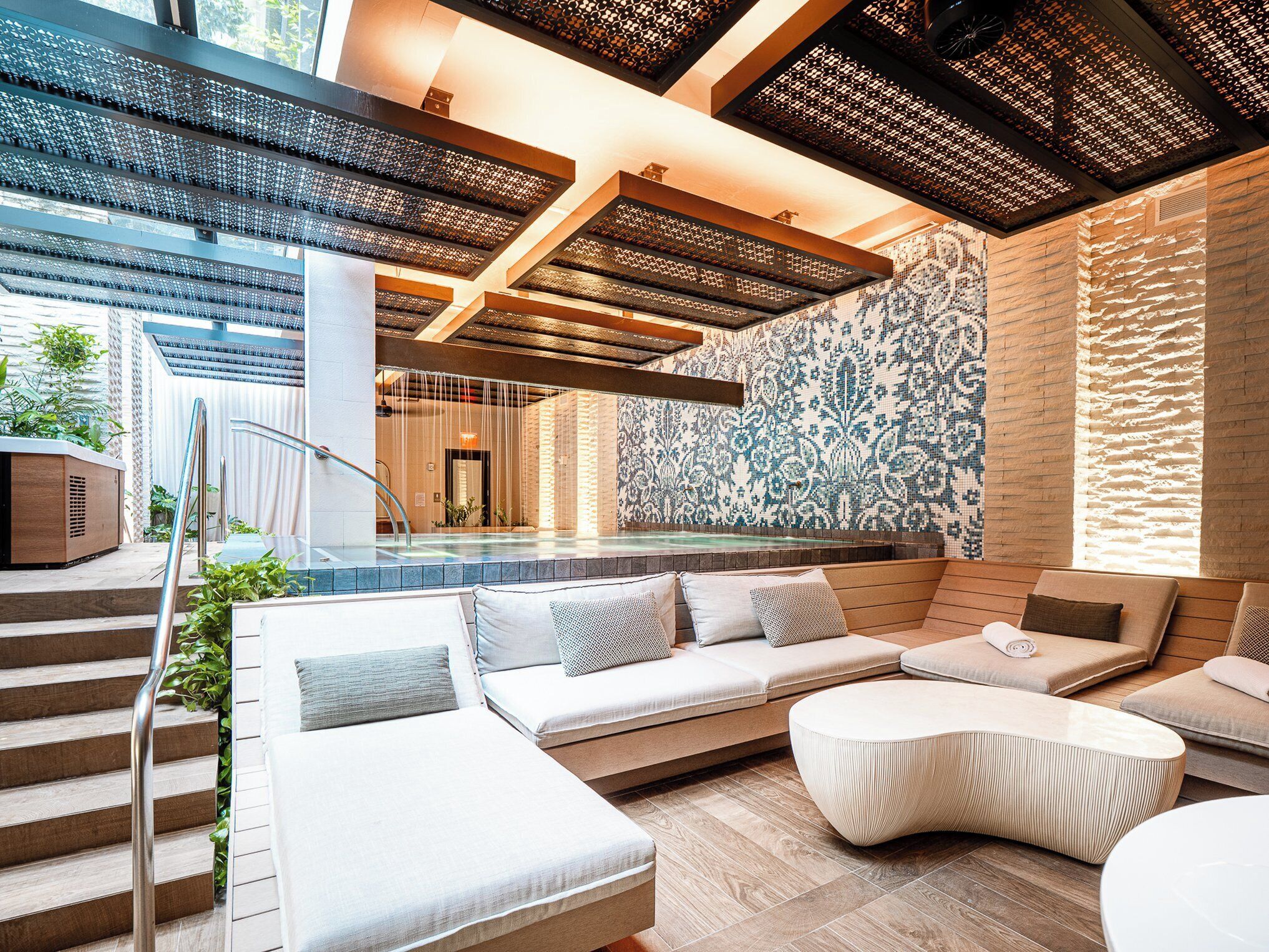 Un área de piscina interior moderna con zona de estar y una escalera.