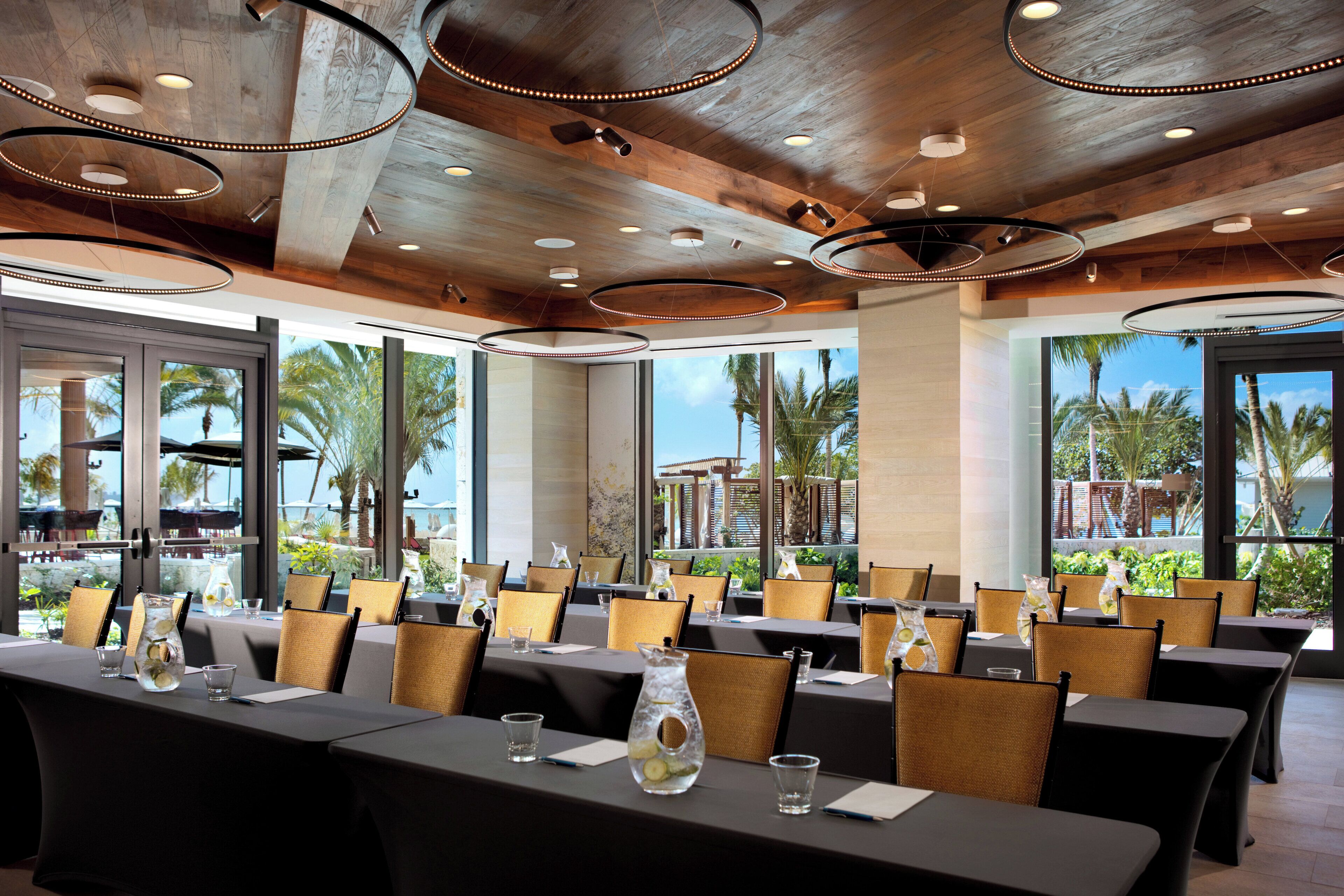 Un salón de conferencias con mesas, sillas y vista a palmeras y una piscina.