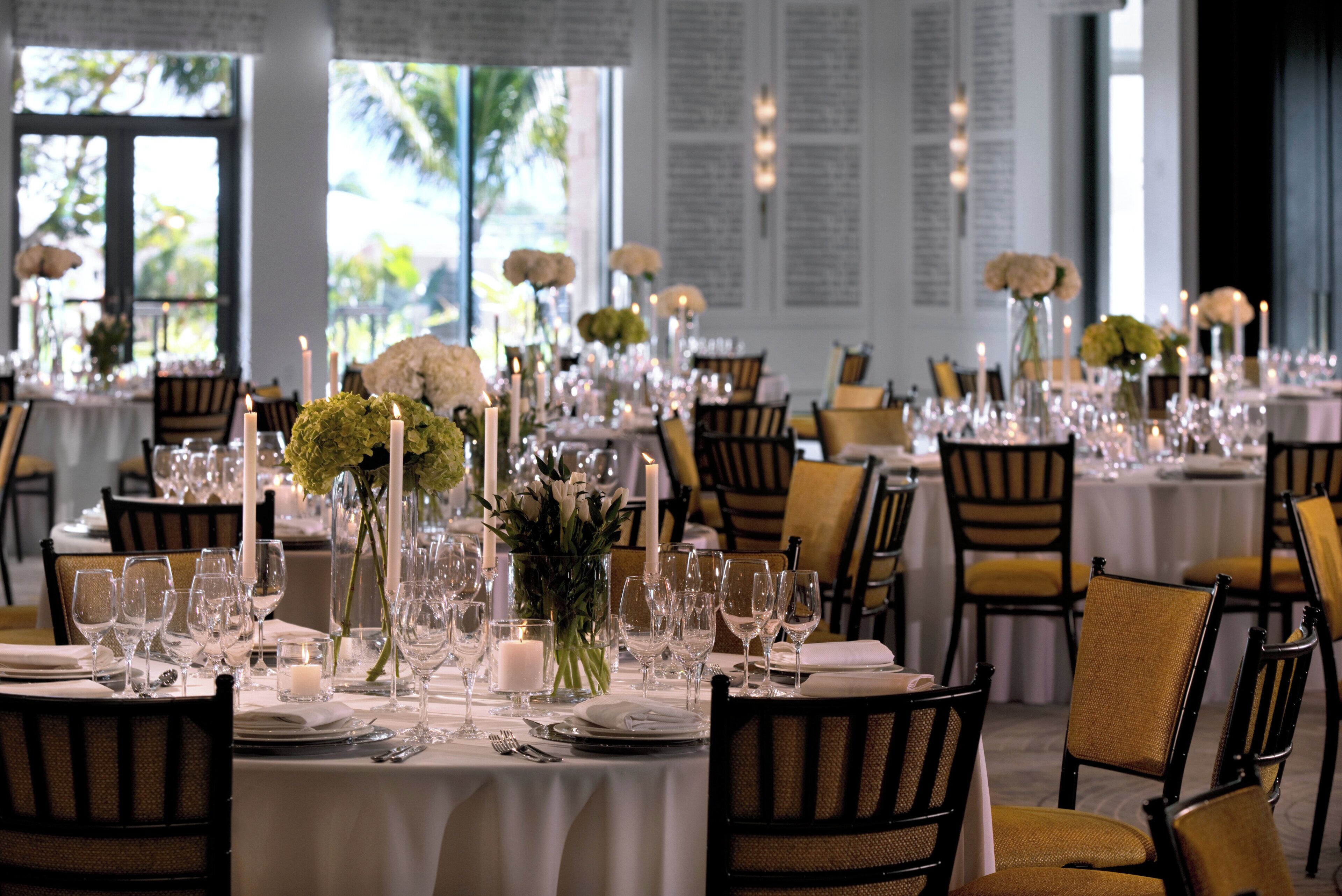 Un comedor formal con varias mesas dispuestas para recibir a comensales, con manteles blancos, velas y centros de mesa con flores.