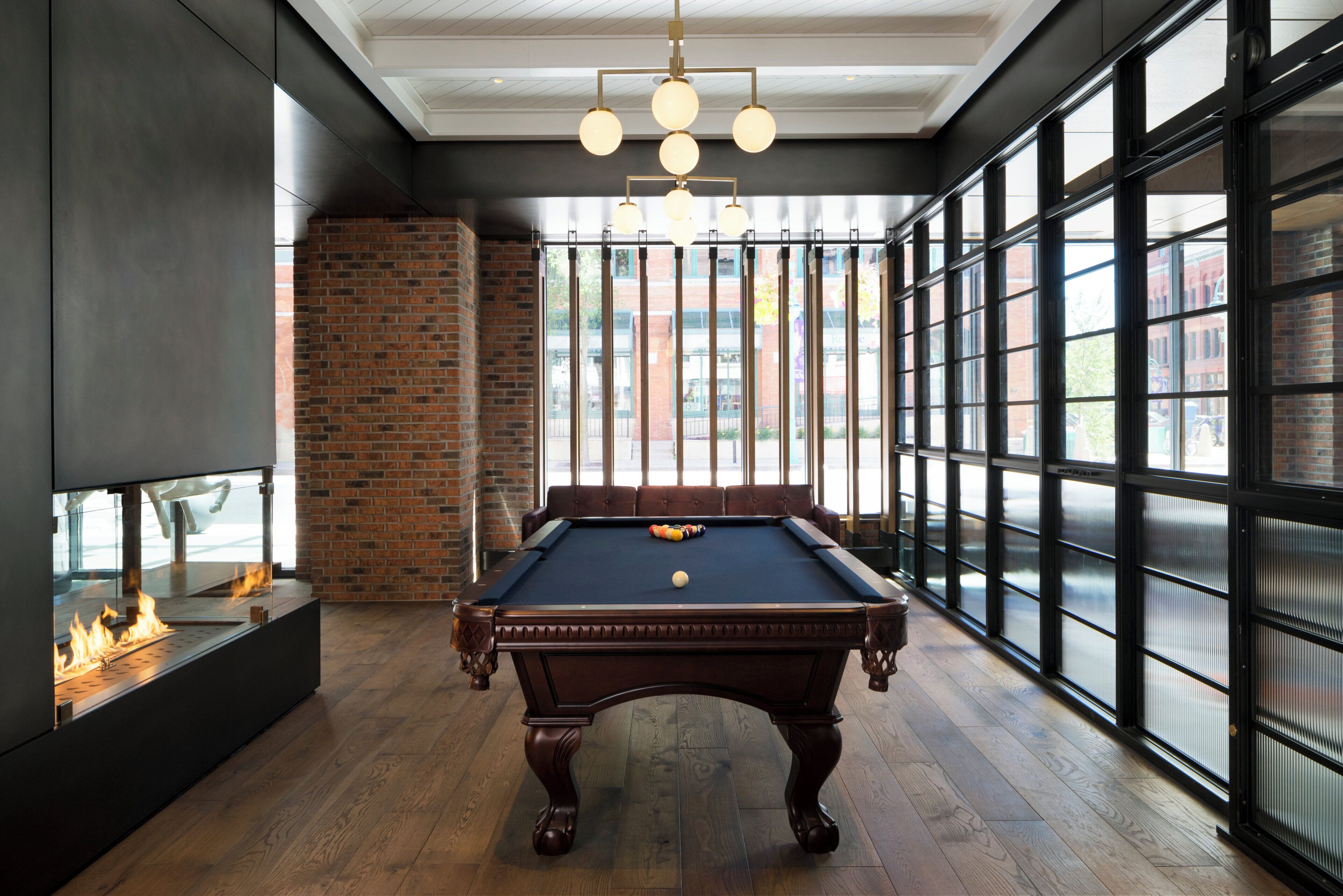A pool table in a room with large windows, a brick wall, and a fireplace.