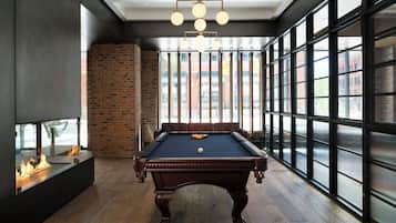 A pool table in a room with large windows, a brick wall, and a fireplace.