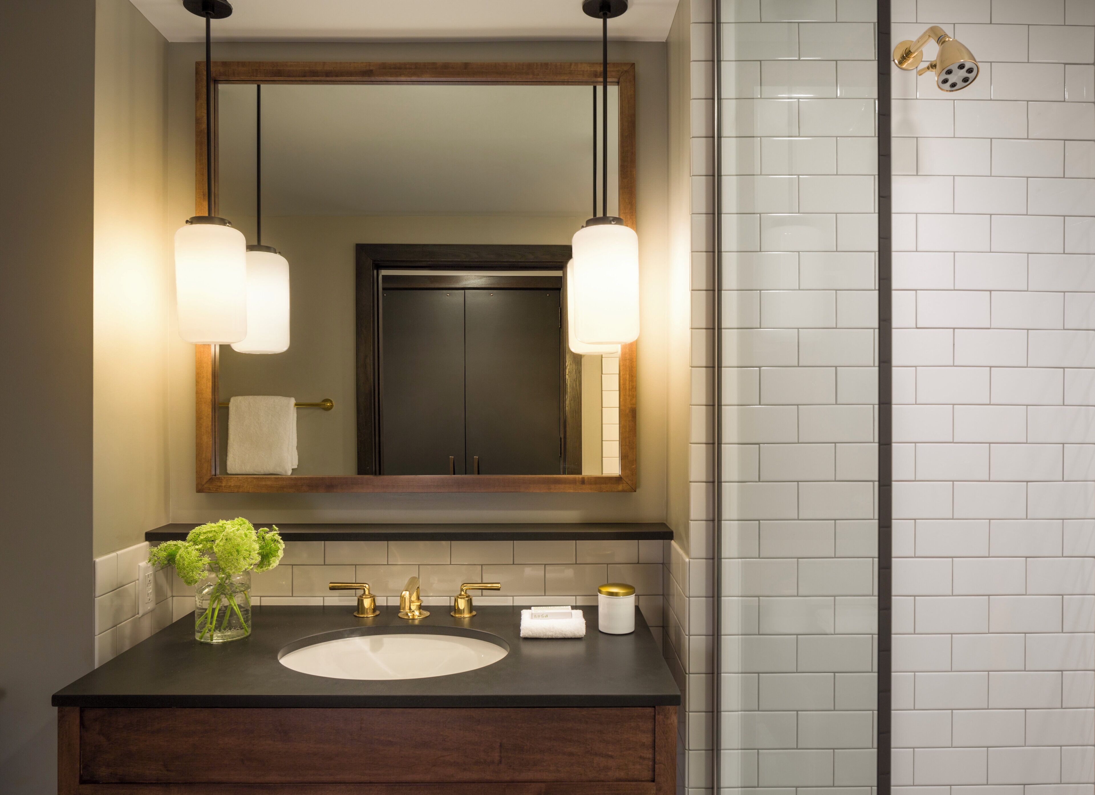 A bathroom with a dark wooden vanity, a white sink, two gold faucets, a mirror with a wooden frame, and a shower with a gold showerhead.