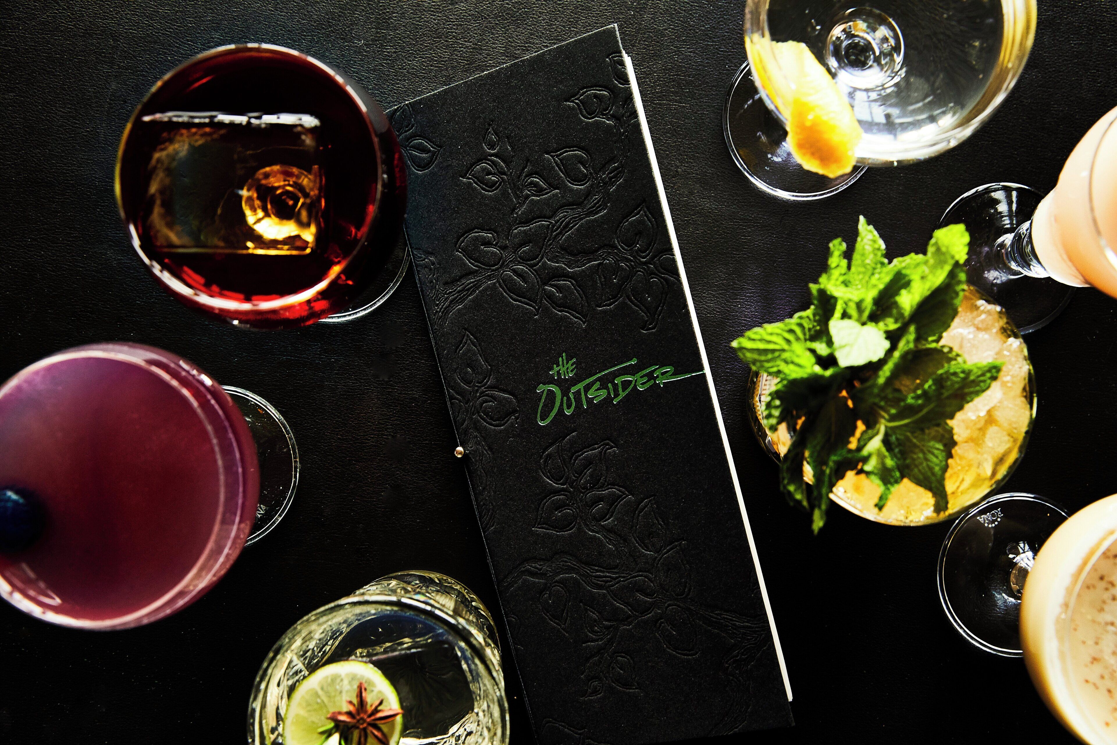A black leather-bound book with embossed floral patterns and the text 'The Outsider' on the cover.