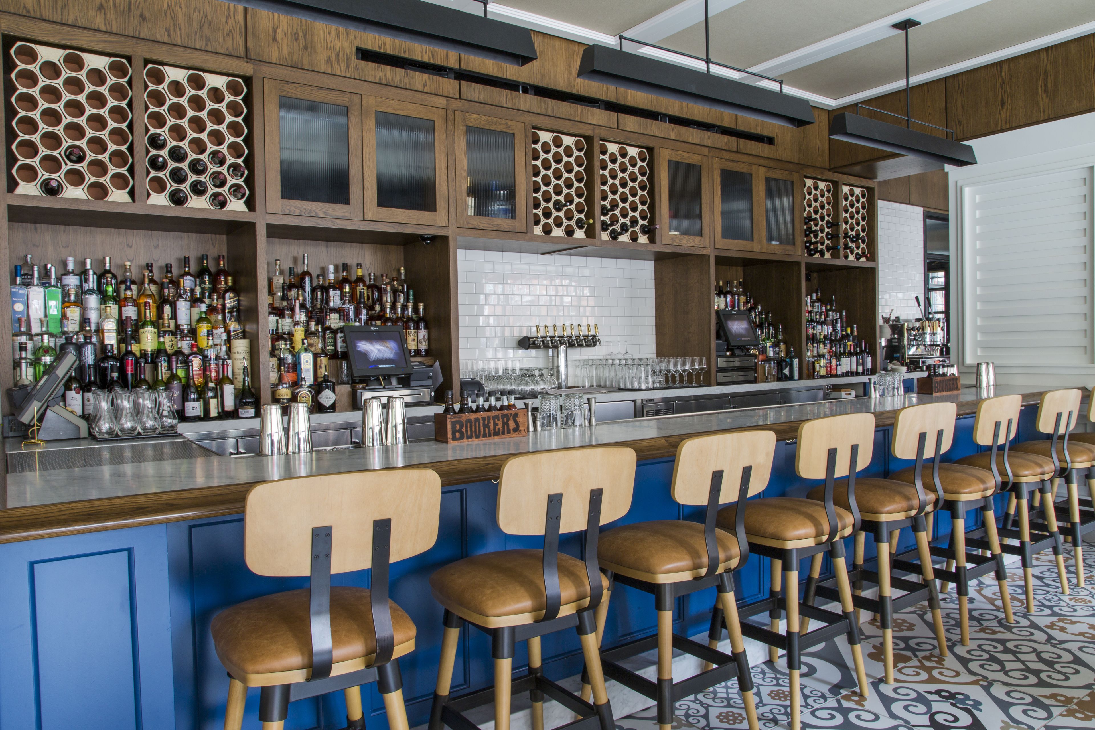A bar area with wooden shelves, bar stools, and a variety of bottles and glasses.