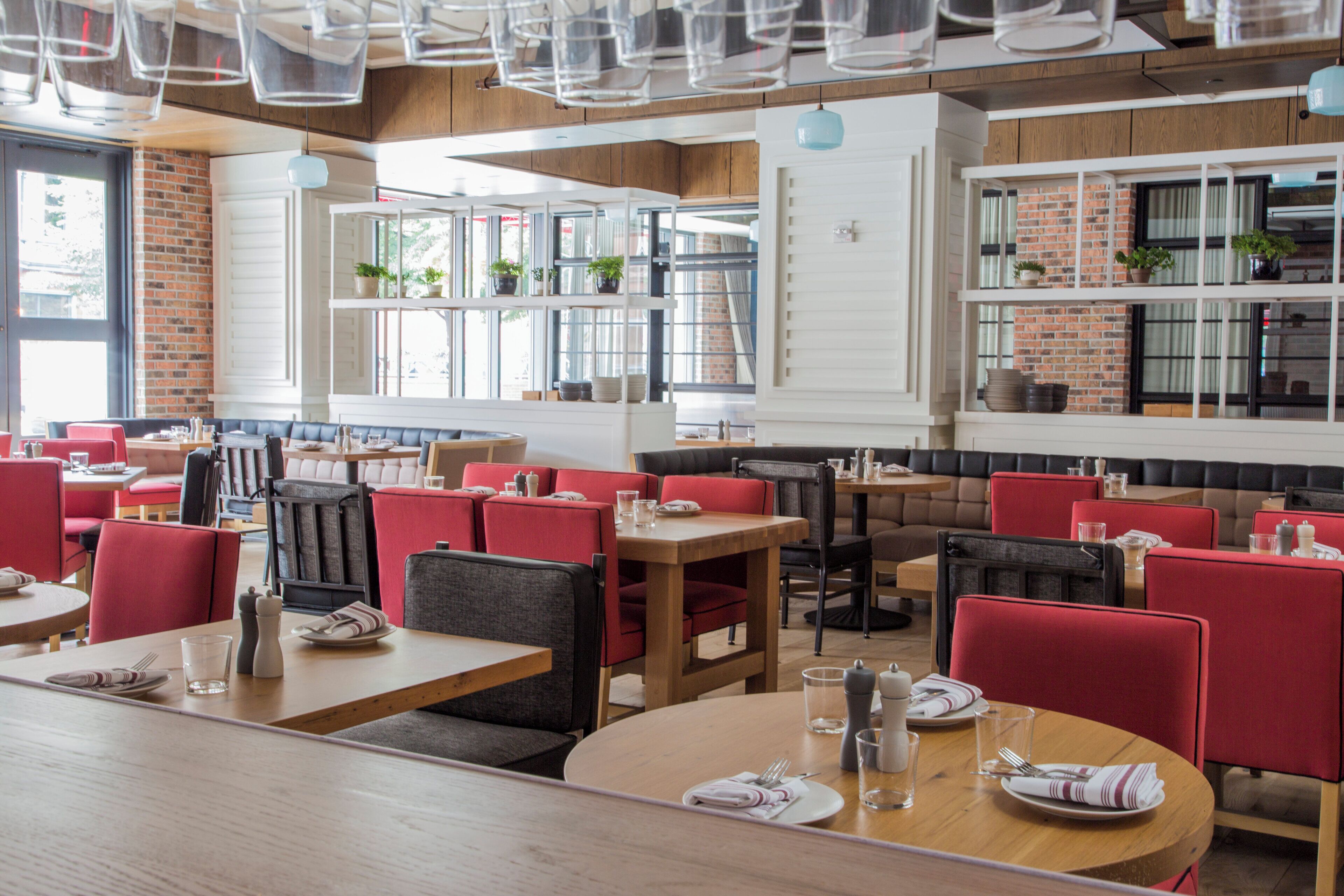 A restaurant with booths and tables, brick walls, and large windows.