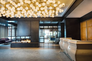 A modern lobby with a fireplace, seating area, and a reception desk. - Kimpton Journeyman Hotel by IHG (Milwaukee)
