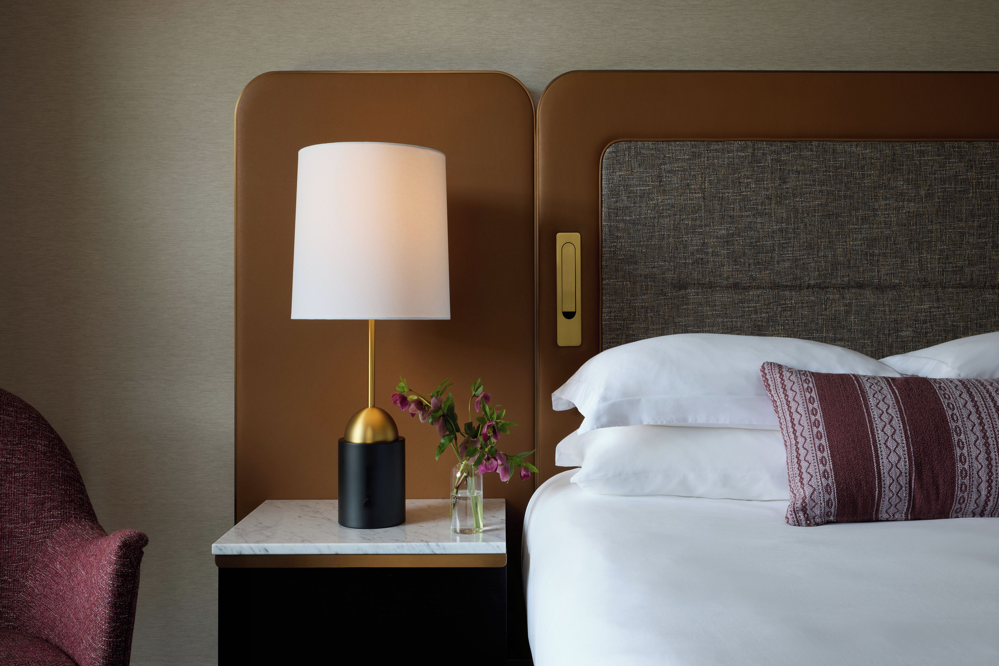 A hotel room with a bed, a nightstand with a lamp, and a vase with flowers.