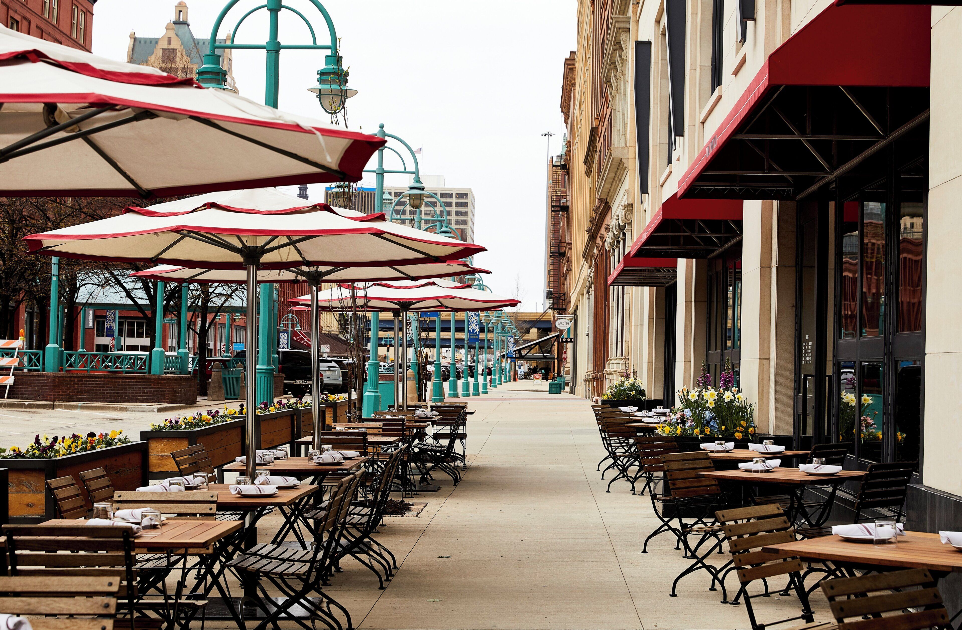 Un café en plein air avec des tables et des chaises, des parasols et une vue sur la rue en arrière-plan.