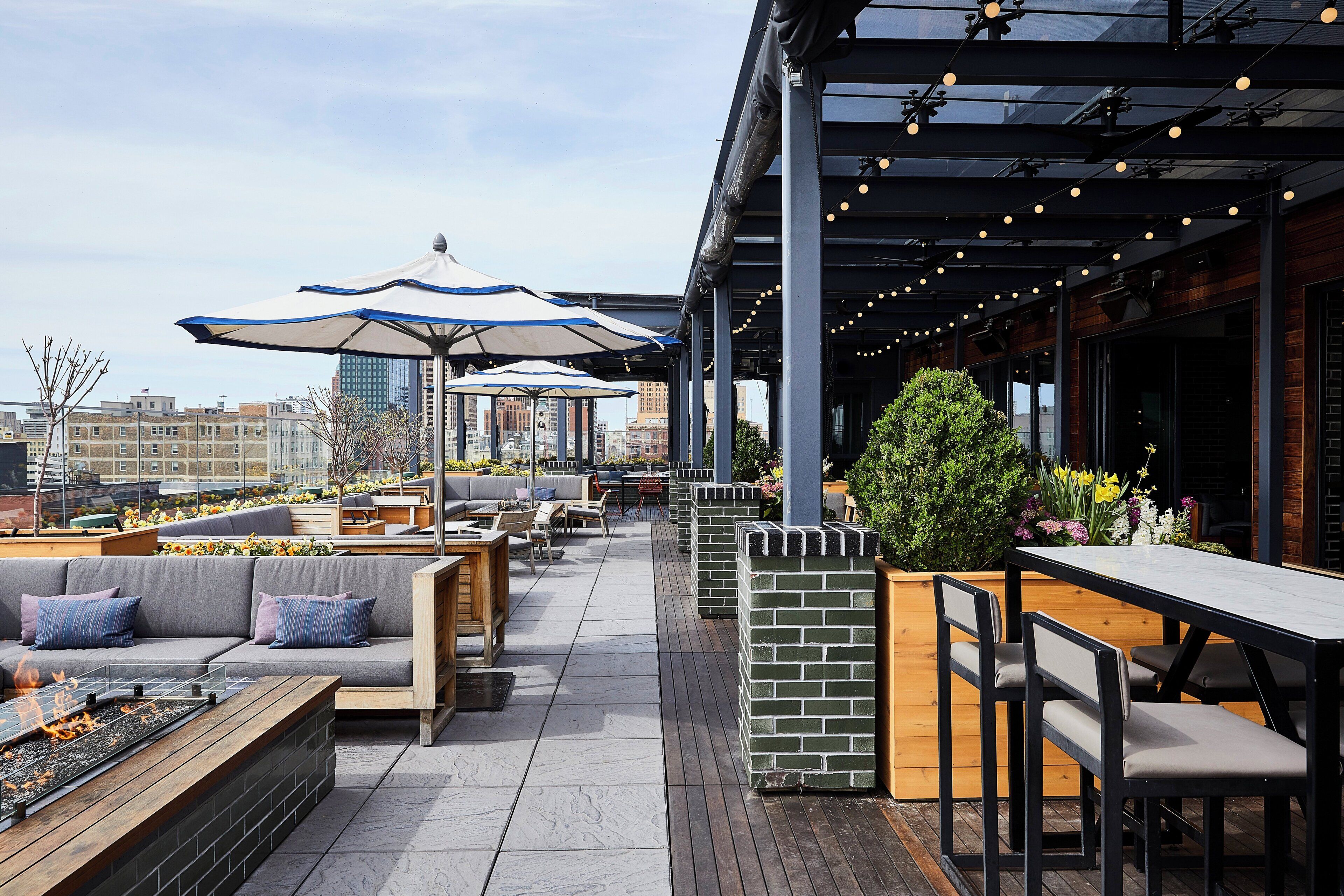A rooftop patio with outdoor seating, umbrellas, and a view of the city skyline.