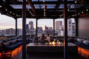 An outdoor seating area with a fire feature, overlooking a cityscape. - Kimpton Journeyman Hotel by IHG (Milwaukee)