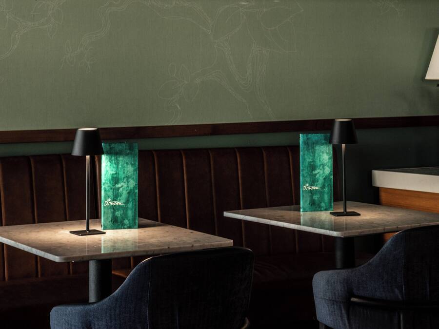 Interior de restaurante con cabinas, mesas y una pared verde con diseño de pizarra.