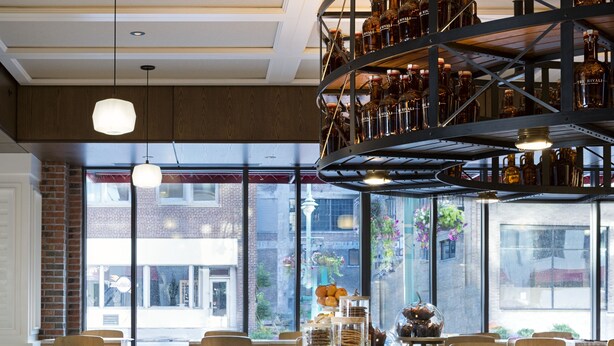 A restaurant with a central counter, seating area, and a display of food items. - Kimpton Journeyman Hotel by IHG (Milwaukee)