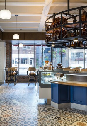 A restaurant with a central counter, seating area, and a display of food items. - Kimpton Journeyman Hotel by IHG (Milwaukee)