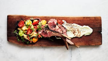 A wooden board with a cooked lamb chop, a salad, and a fried egg.