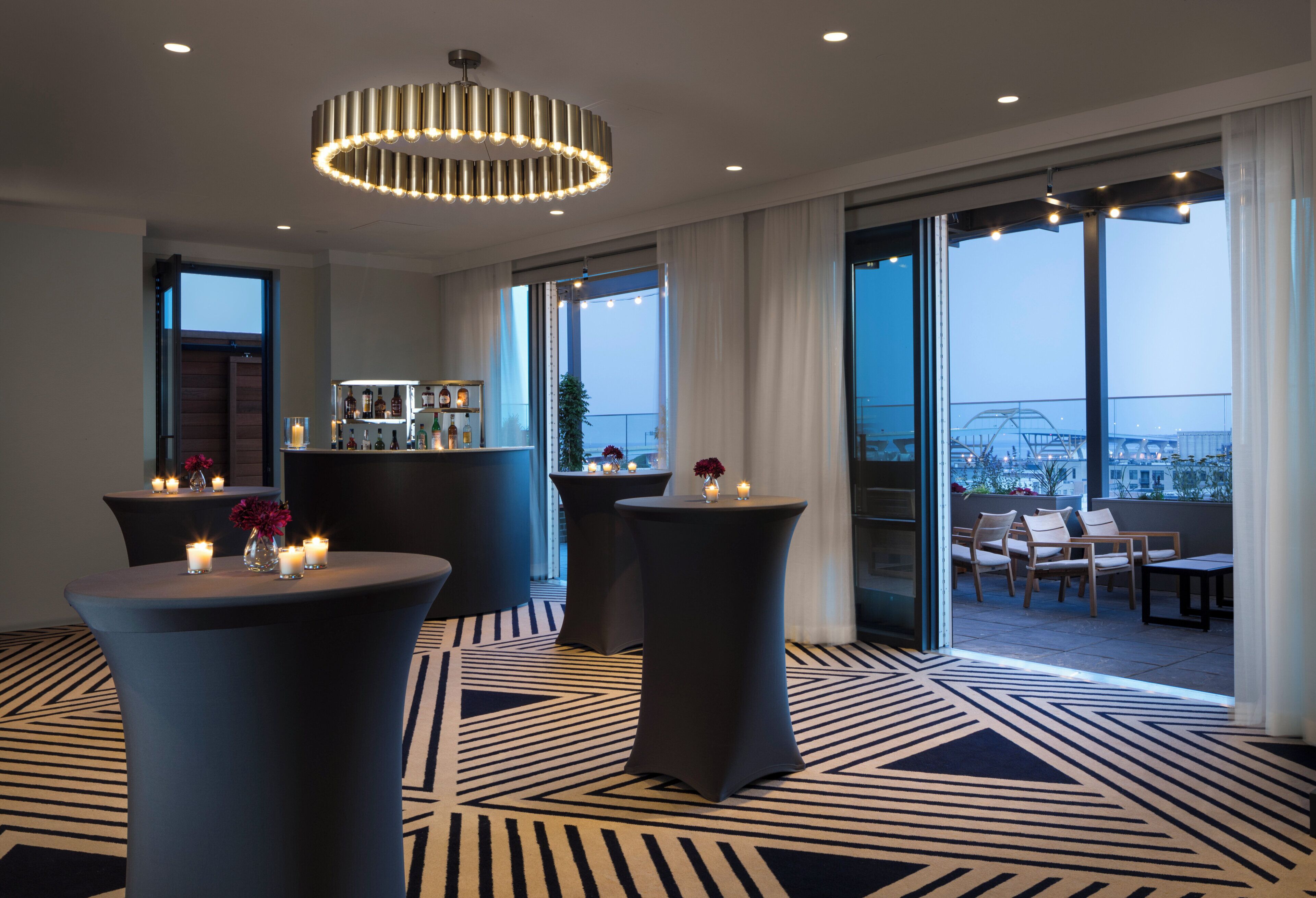 Een moderne hotellobby met ronde tafels, een bar en grote ramen met uitzicht over de stad.