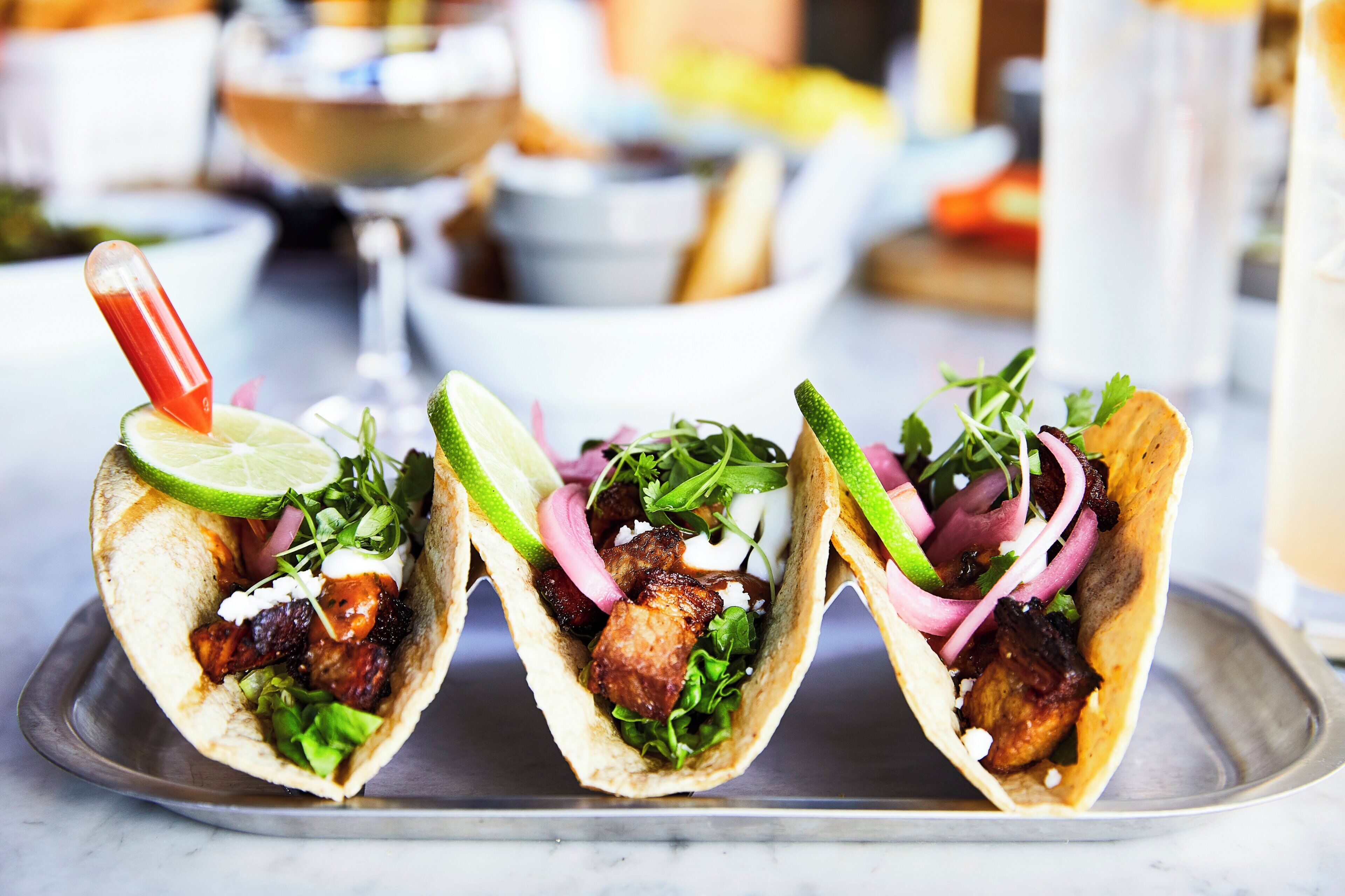 Drie taco's met diverse toppings op een metalen schaal.