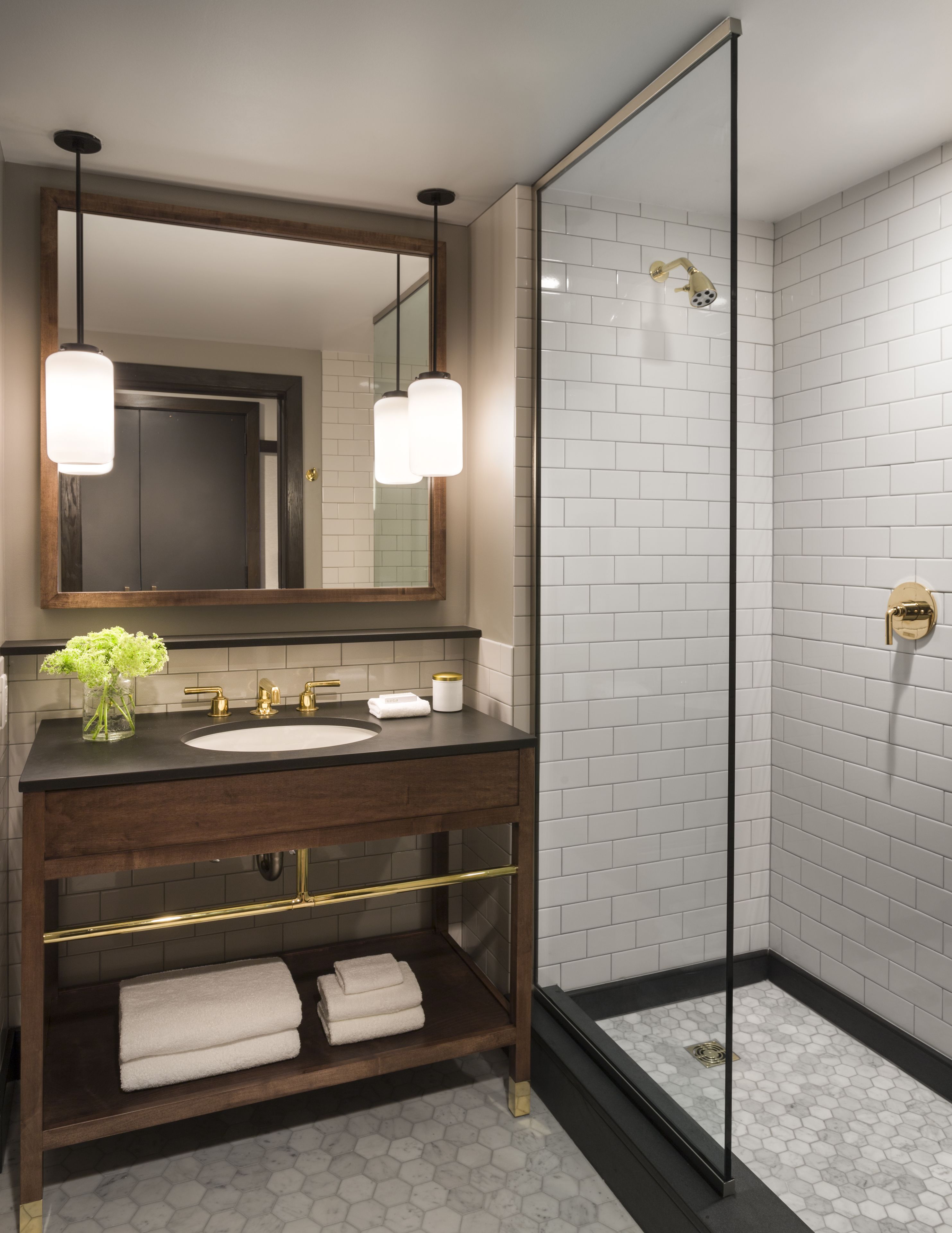 A modern bathroom with a dark wooden vanity, a large mirror, a glass-enclosed shower, and white hexagonal tiles.