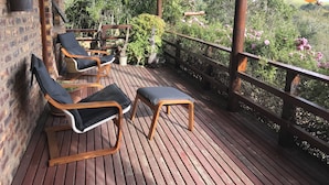 A wooden deck with four lounge chairs, a small table, and a railing overlooking a lush garden. - The Carraighs (The Crags)