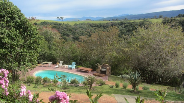A pool with lounge chairs and a barbecue area surrounded by lush greenery and hills in the background. - The Carraighs (The Crags)