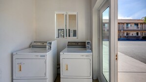 Two front-loading washers in a laundry room with a view of a parking lot and a building in the background. - Hotel Galaxy (Las Vegas)