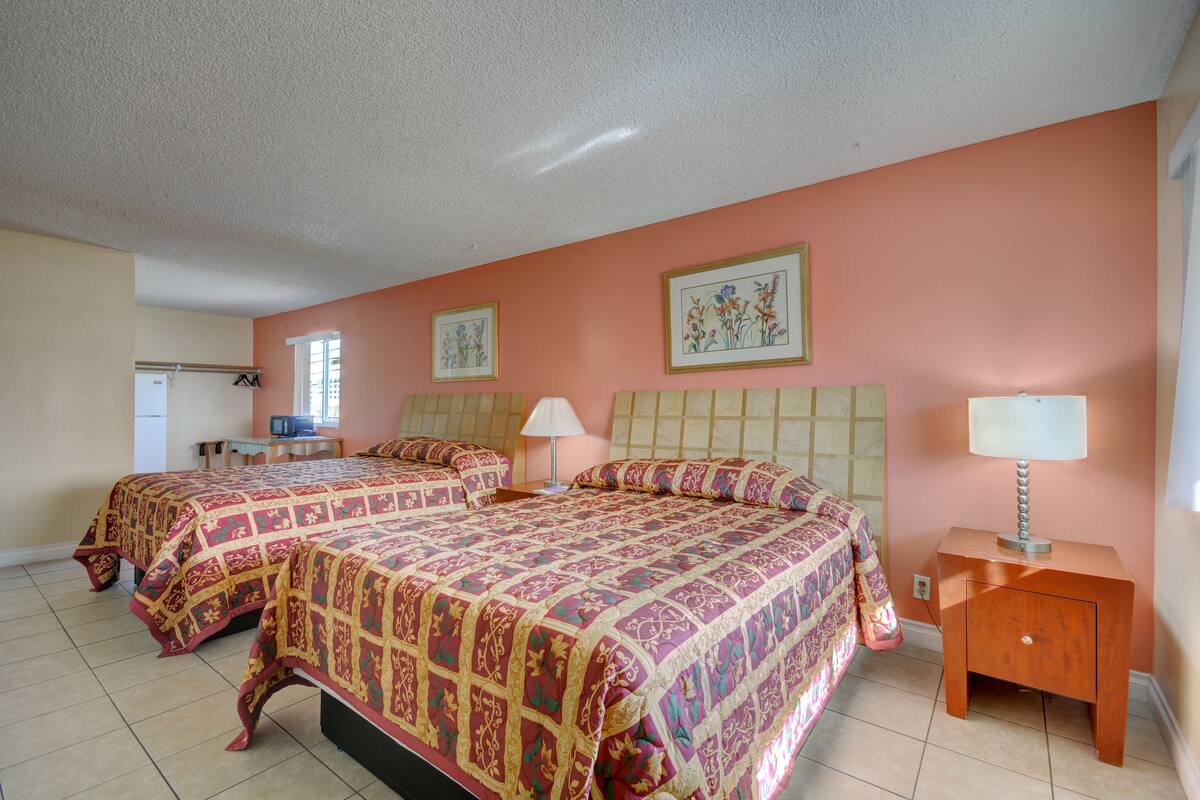 A bedroom with two beds, a nightstand with a lamp, and a dresser.