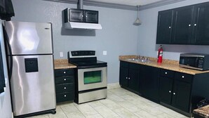 A compact kitchen with a stainless steel refrigerator, an oven, a microwave, and black cabinets. - Hotel Galaxy (Las Vegas)