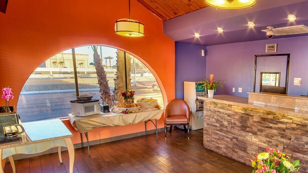 A reception area with a stone counter, a large arched window, and a seating area with a chair and table. - Hotel Galaxy (Las Vegas)