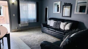 A living room with a black leather sofa, a small table, and a large window with sheer curtains. - Hotel Galaxy (Las Vegas)