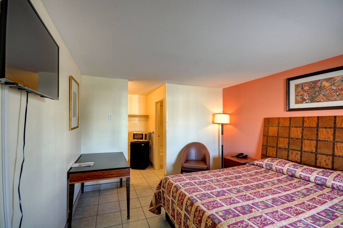 A hotel room with a bed, a desk, a chair, a TV, and a lamp.