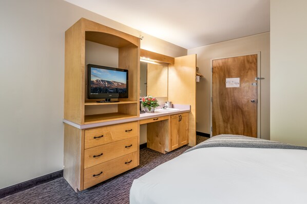 A hotel room with a wooden desk, a television, a bed, and a door.