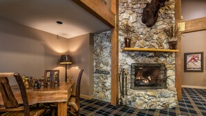 A dining area with a wooden table and chairs, a fireplace, and a stone wall.