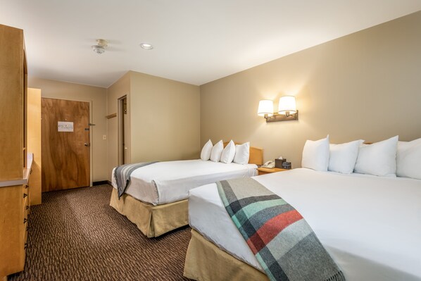 Habitación de hotel con dos camas, un armario de madera, piso alfombrado y una lámpara fijada a la pared.