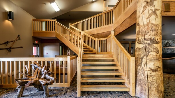 A wooden staircase with a railing, a wooden bench, and a large wooden pillar with animal carvings.