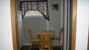 A small dining area with a table and four wooden chairs, a window with a decorative curtain, and a starfish decoration on the wall. - Jeddore Lodge Cabins (Head of Jeddore)