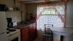 A compact kitchen with a stove, microwave, and sink. There is a small table and a chair. - Jeddore Lodge Cabins (Head of Jeddore)