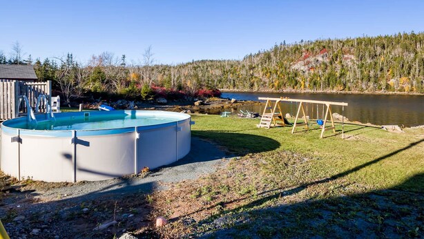 Ein Garten mit Swimmingpool, Holzschaukel und einem von Bäumen umgebenen See.