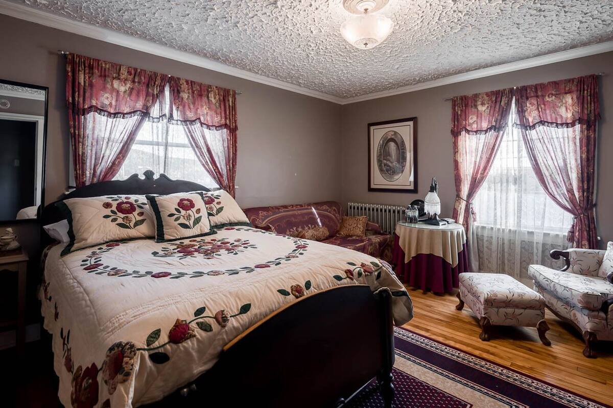 A bedroom with a large bed, a small table, a chair, and a radiator.