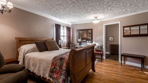 Ein Schlafzimmer mit einem hölzernen Bett, einem Sessel, einem Spiegel und einer Heizung.