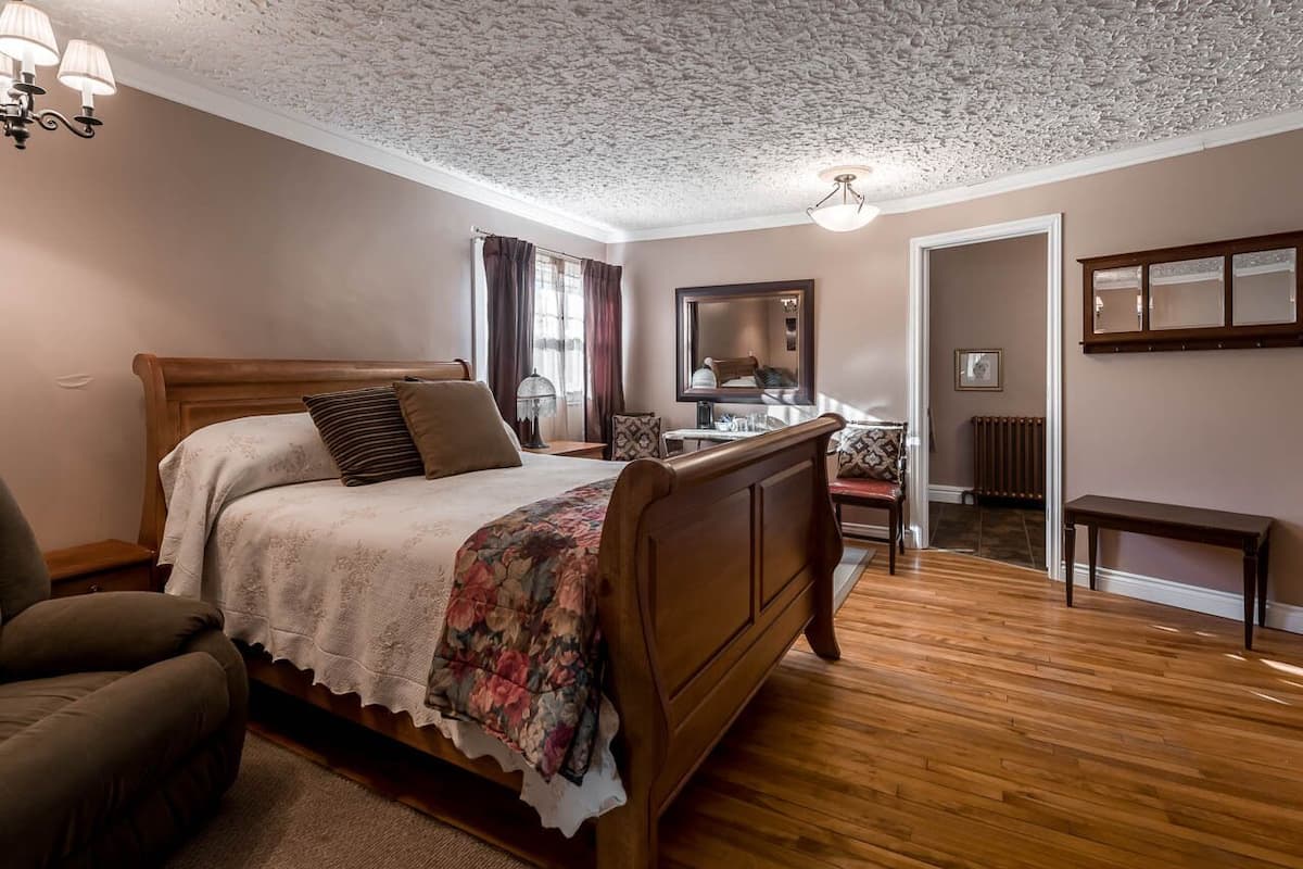 A bedroom with a wooden bed, a chair, a mirror, and a radiator.