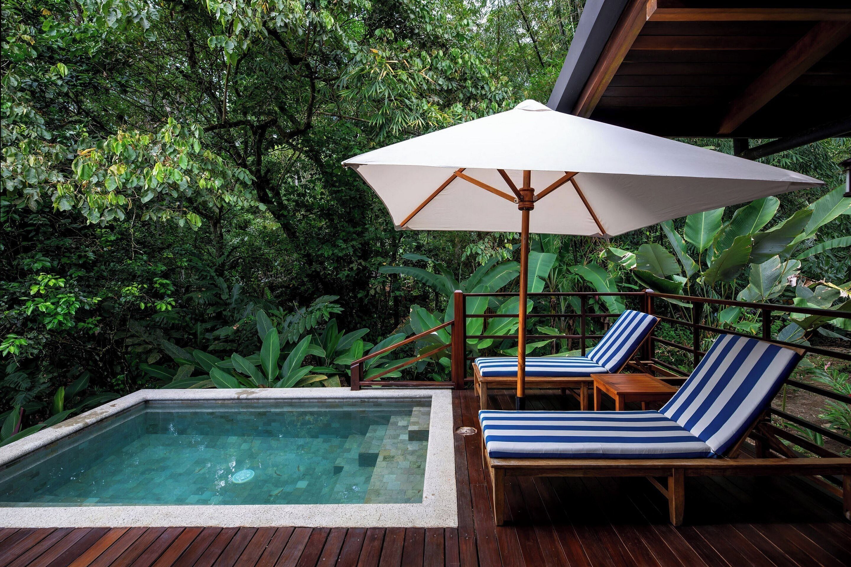 A wooden deck with a hot tub, lounge chairs, and an umbrella.