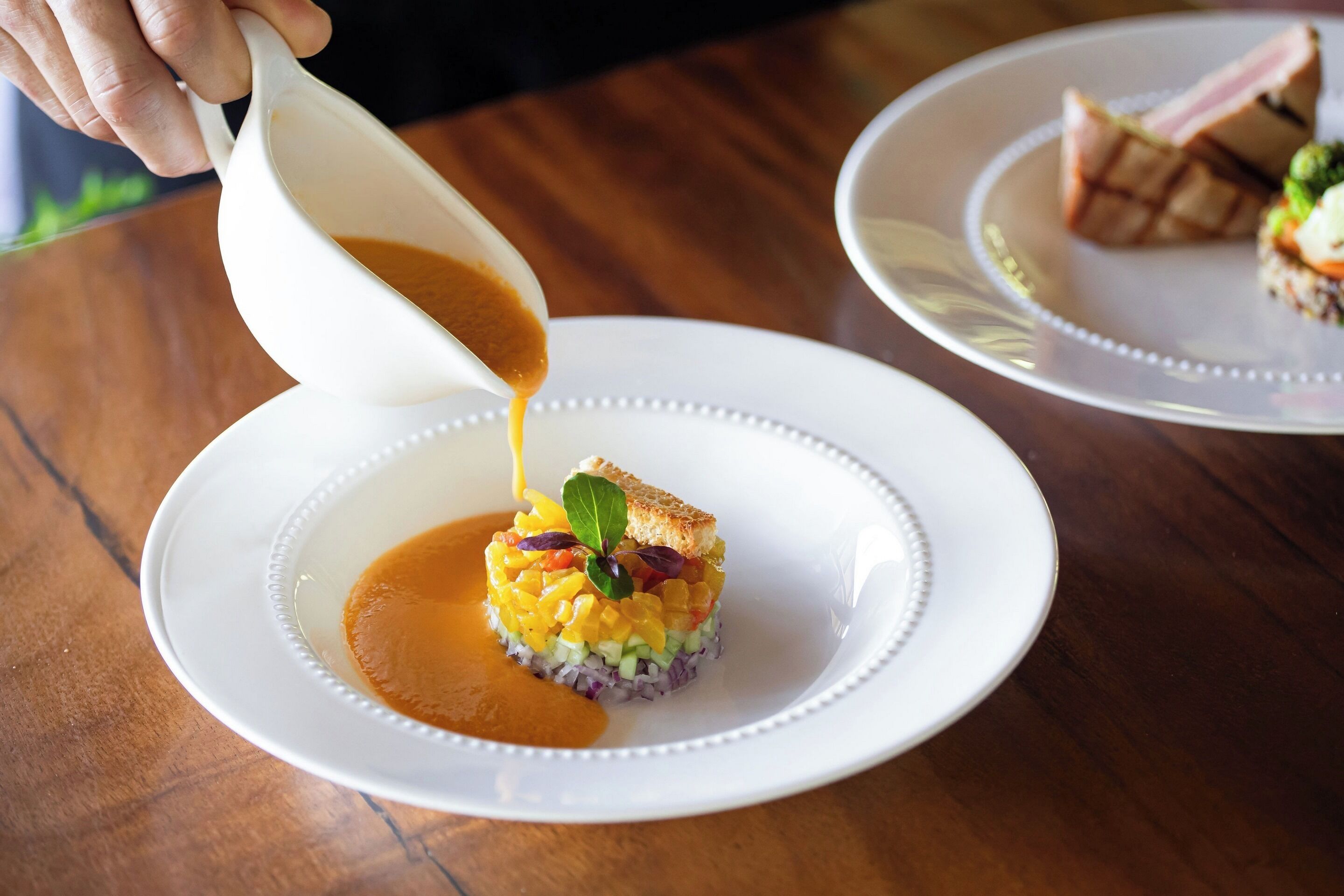 A person pouring sauce onto a dish with a garnish.