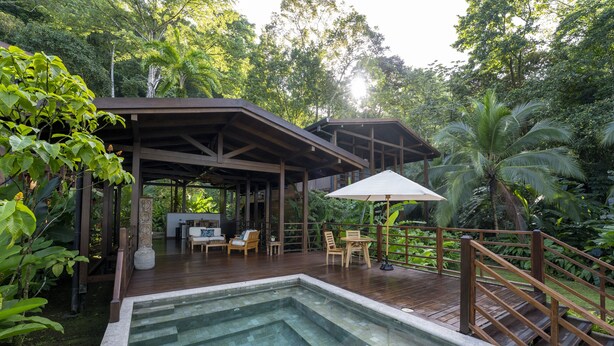 A pool area with a wooden deck, lounge chairs, and a covered seating area surrounded by lush greenery. - Playa Cativo Lodge (Golfito)