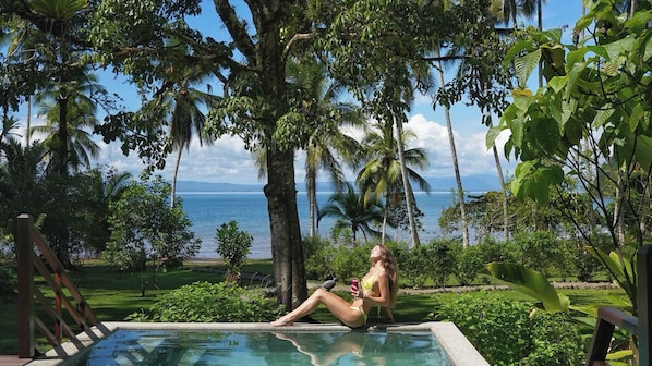Eine Frau sitzt am Pool mit Blick auf den Ozean und Palmen.