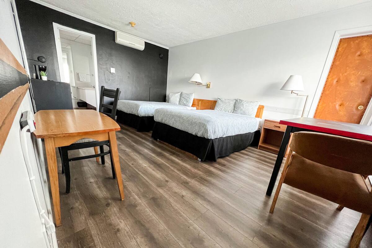 Ein Hotelzimmer mit zwei Betten, einem Holztisch, einem Schreibtisch und einem Stuhl.
