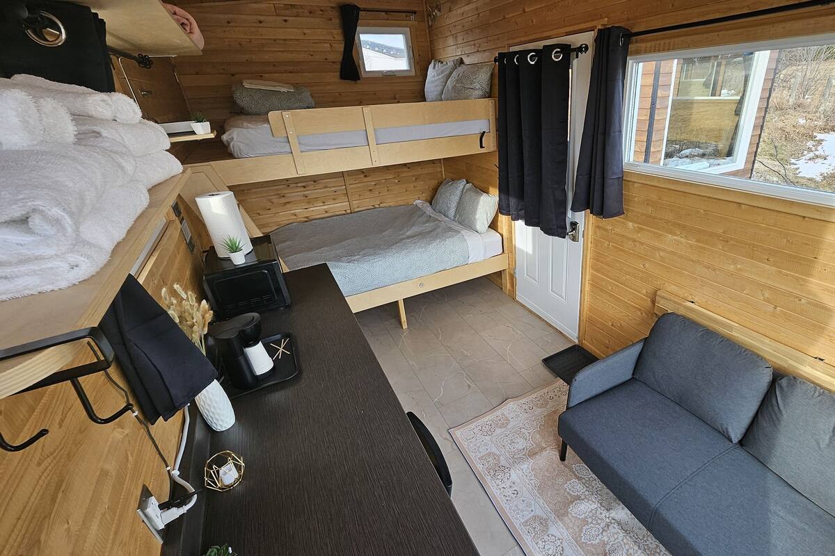 Ein gemütliches Blockhaus-Interieur mit Etagenbett, einer Couch, einem kleinen Tisch mit Kaffeemaschine und einem Fenster mit Blick auf eine verschneite Landschaft.