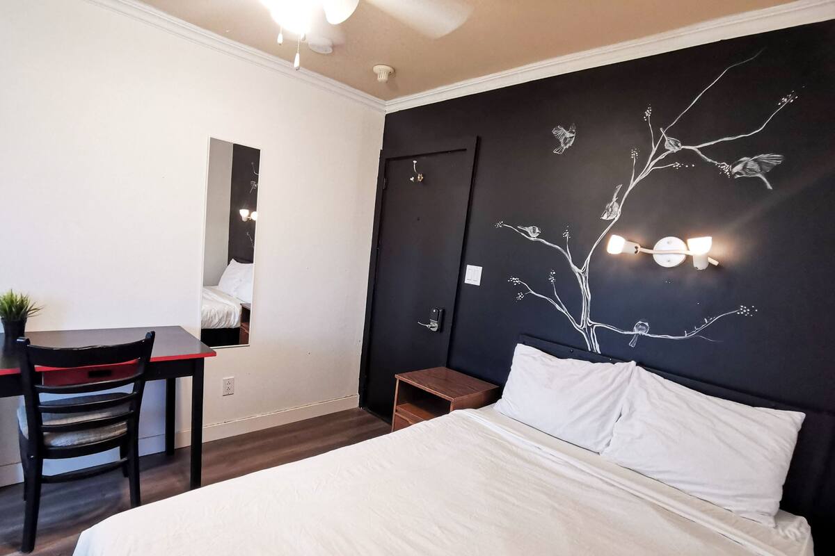 Ein Hotelzimmer mit Bett, Schreibtisch, Stuhl und einer Wand mit einem Baum-Wandbild.