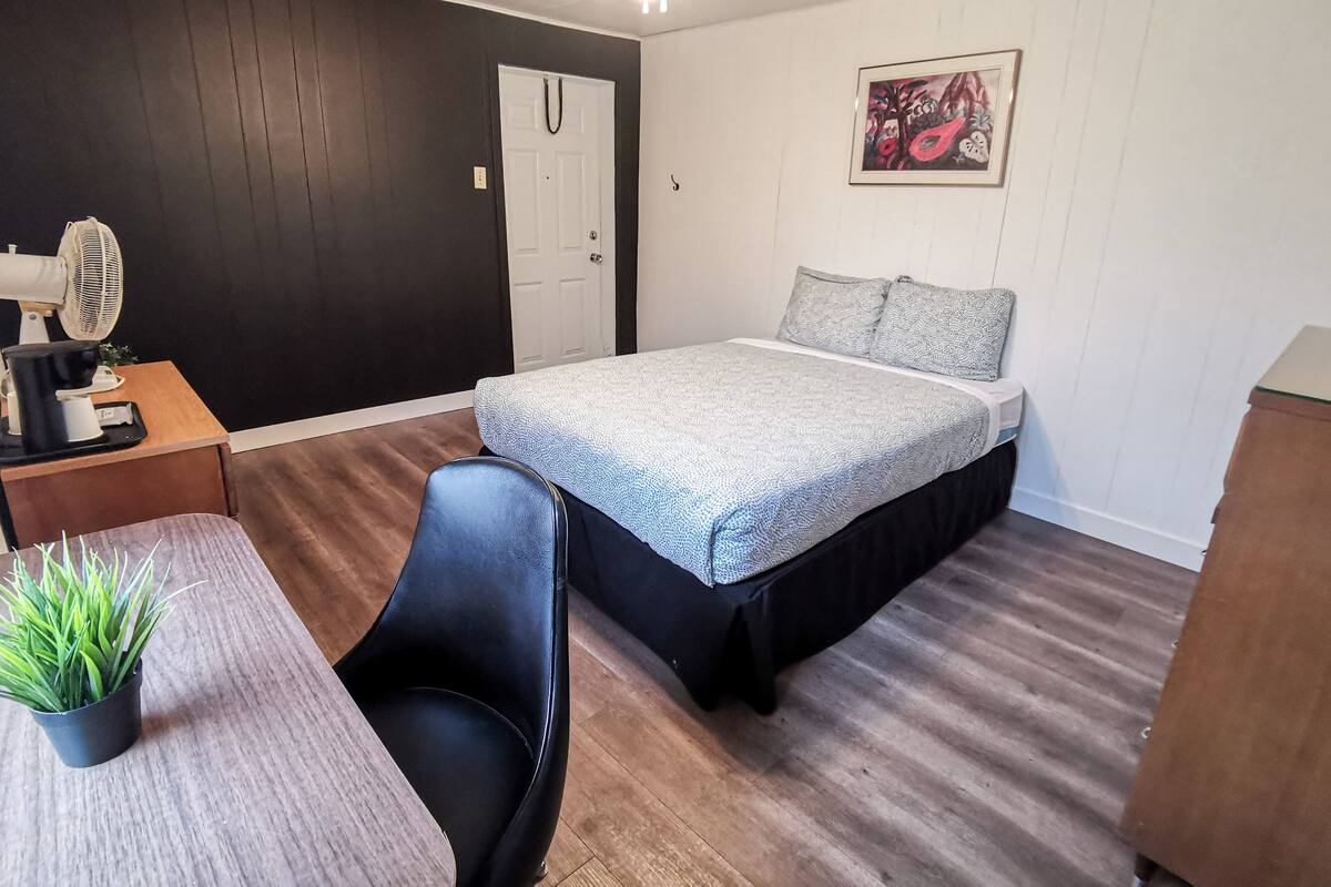 Ein Schlafzimmer mit einem Bett, einem Schreibtisch mit Stuhl, einem Ventilator und einer Topfpflanze.