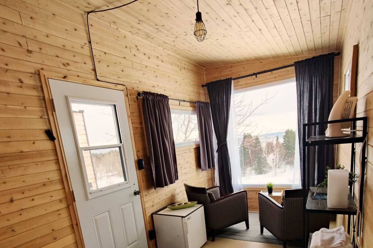 Ein gemütliches Zimmer mit einem Bett, einem kleinen Tisch, einem Sessel, einem Fenster mit Vorhängen und einem Regal mit Handtüchern.